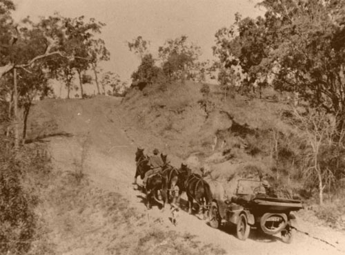 An early Model T Ford being towed up the steep hill by a team of horses
